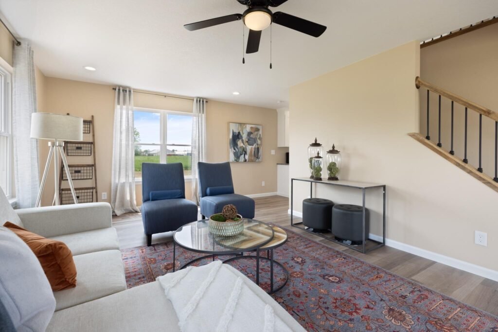 Living room with beige walls, blue chairs, a sofa, glass coffee table, and staircase railing
