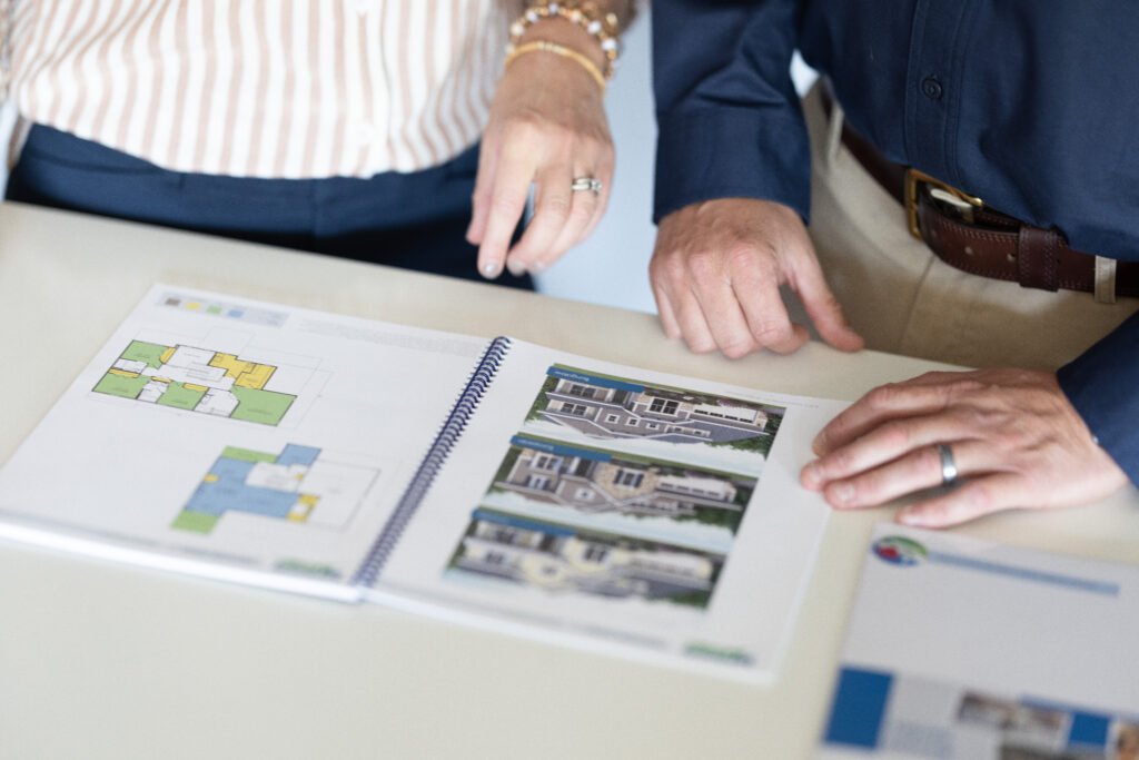 People reviewing house floor plans and exterior design mockups in a brochure