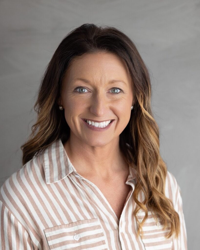 Portrait of a smiling woman with long brown hair against a gray background