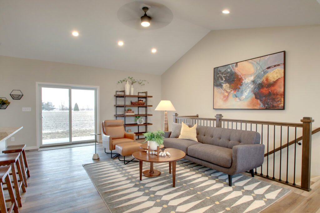 Modern living room with gray sofa, tan chair, abstract wall art, and a lake view through sliding doors