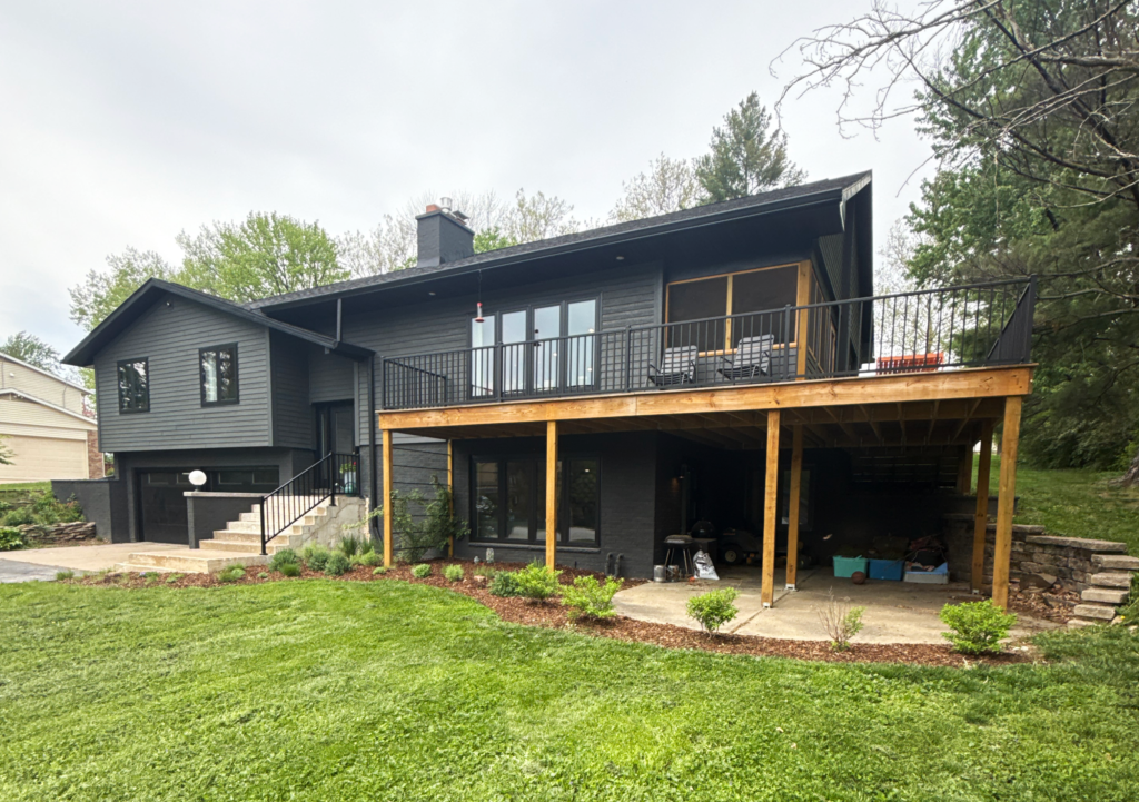 Dark gray two-story house with a large raised deck, covered patio, and green lawn