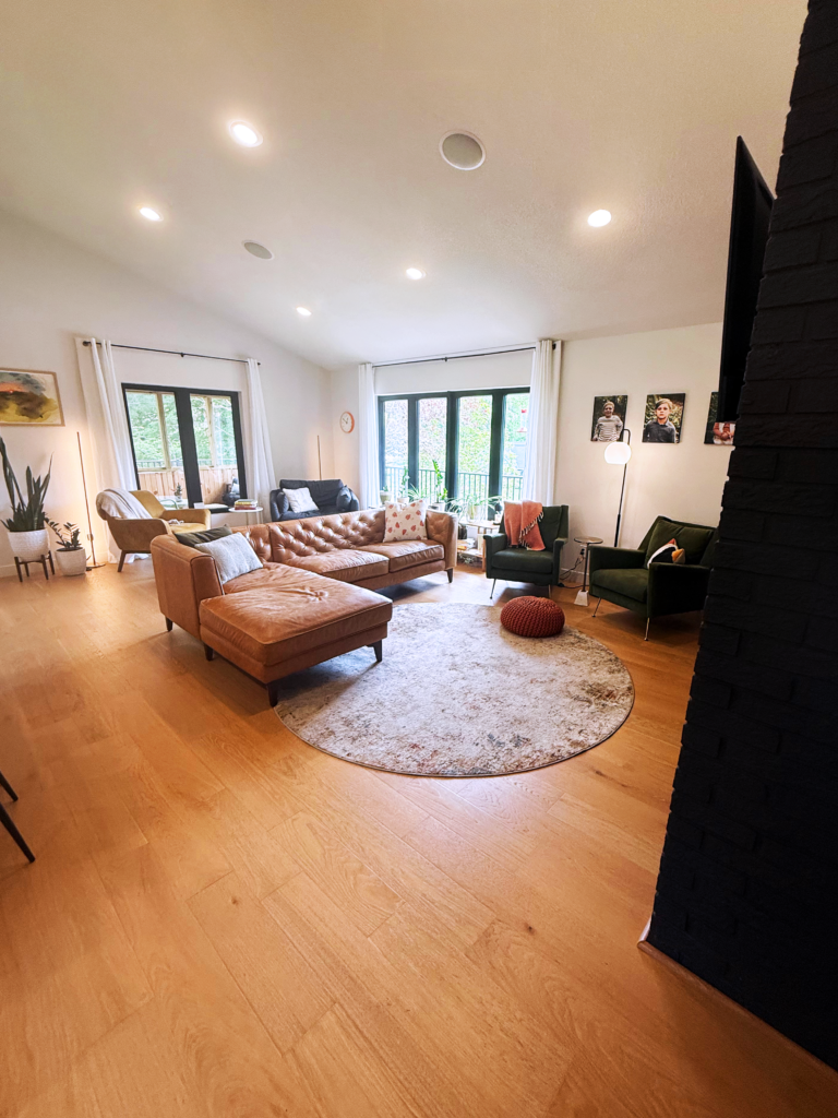 Bright living room with leather sectional, green chairs, large windows, and wood floors