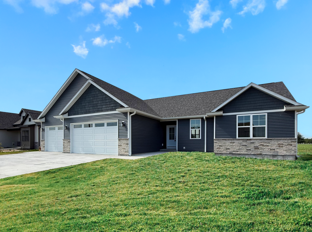 Suburban house with a two-car garage and a large front lawn under a blue sky