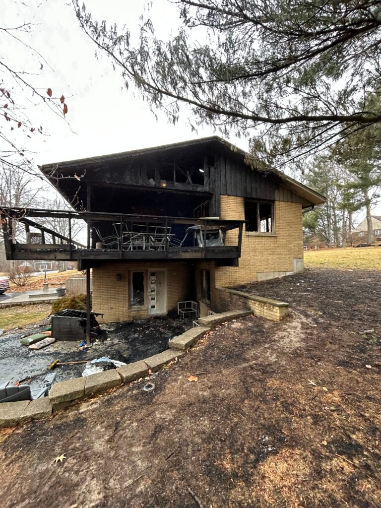Fire-damaged two-story house with a burned upper floor and charred deck