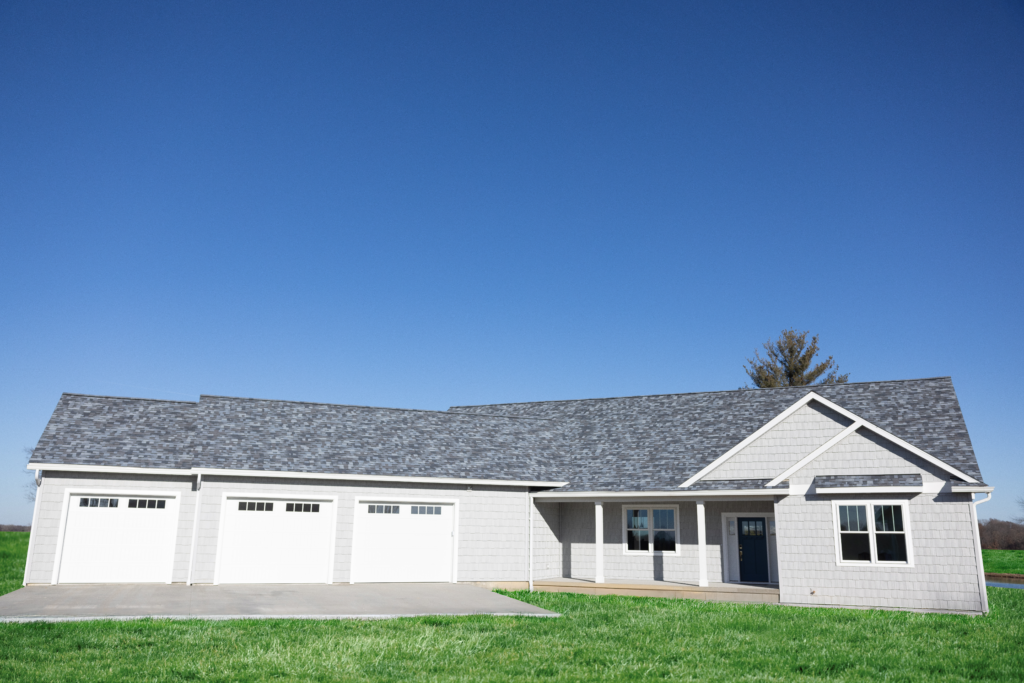 A newly built white house with three garage doors and a front porch under a clear blue sky