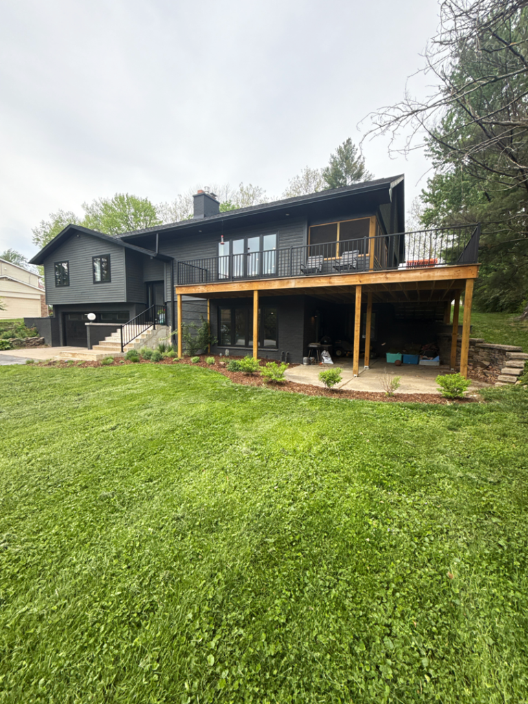 Modern dark-gray house with a large raised deck and a covered patio over a green lawn