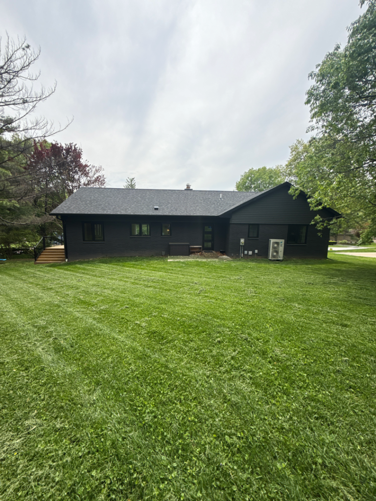 Back of a dark house with a large mowed lawn and trees around it