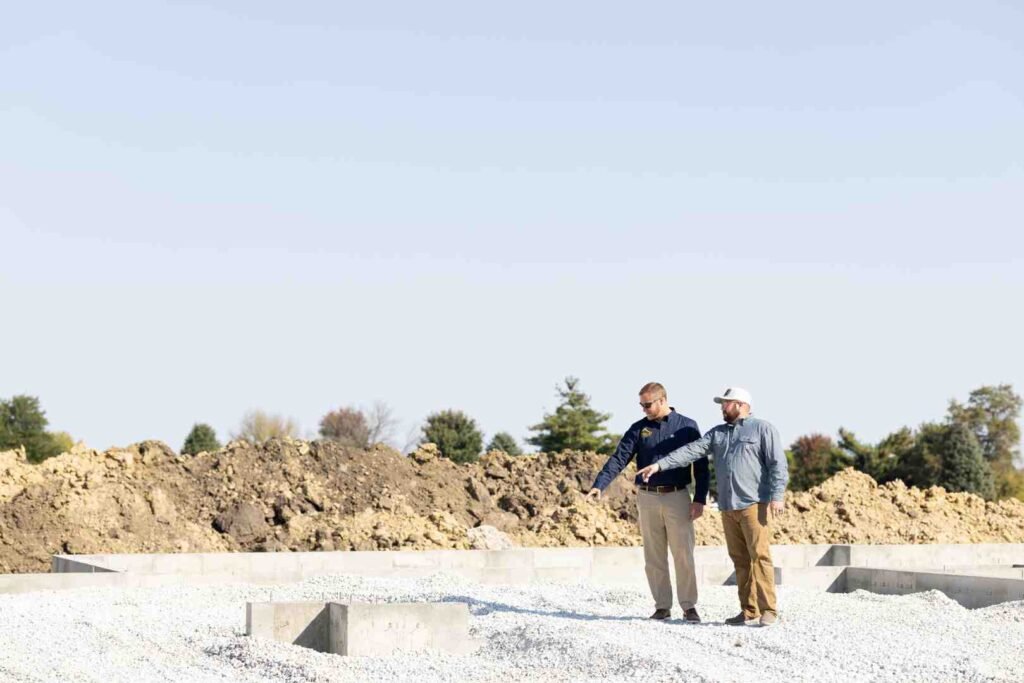 Two men inspect a gravel foundation at a construction site