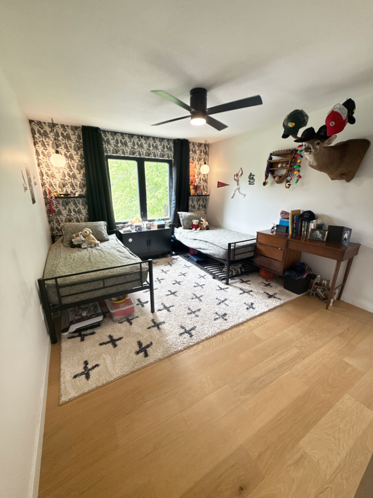 A bedroom with two twin beds, a window, a desk, and mounted deer head decor on the wall