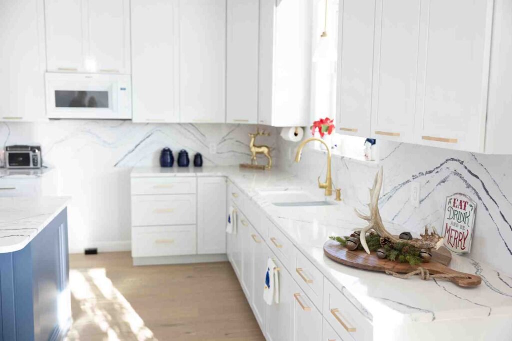 Bright white kitchen with gold fixtures, marble countertops, and a holiday centerpiece on the island