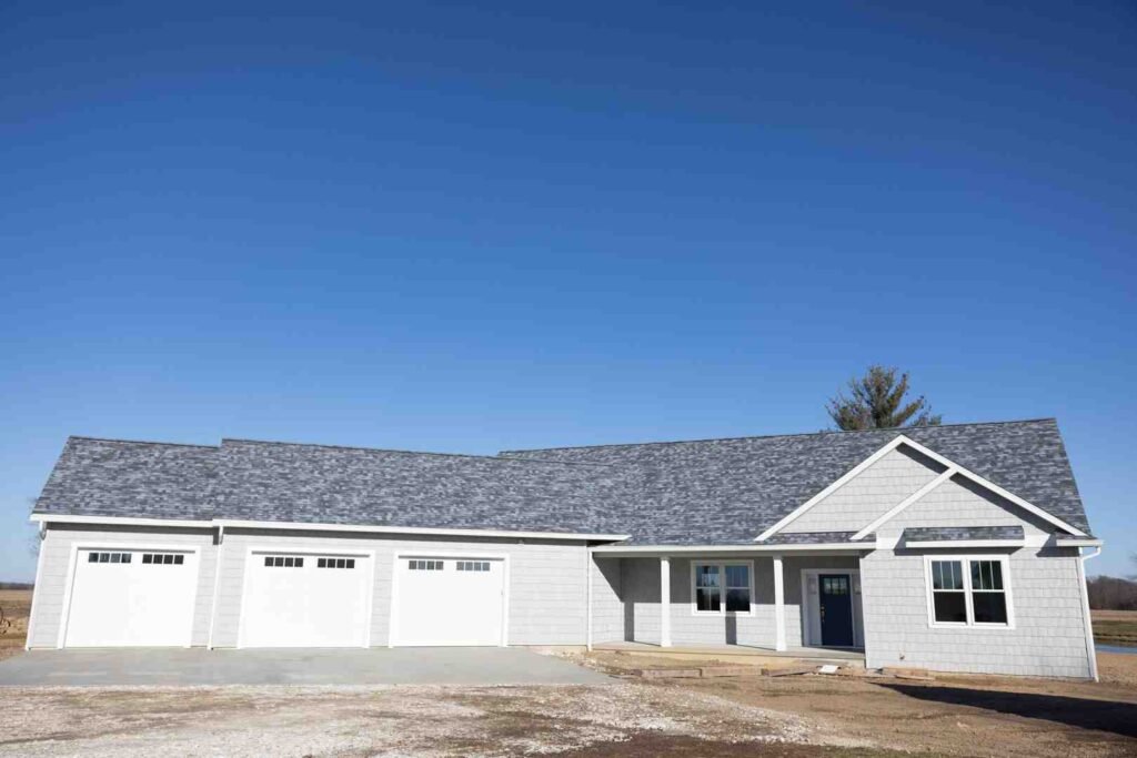 A newly built white house with three garage doors and a front porch under a clear blue sky