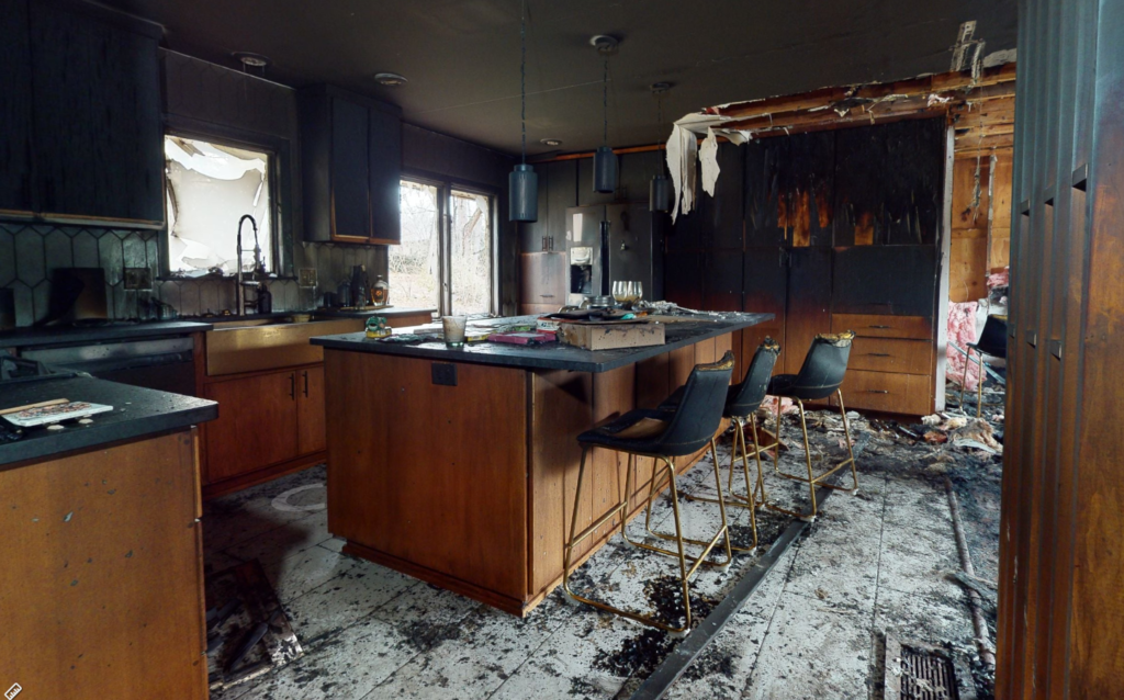 Fire-damaged kitchen with burned cabinets, scorched walls, and debris on the floor