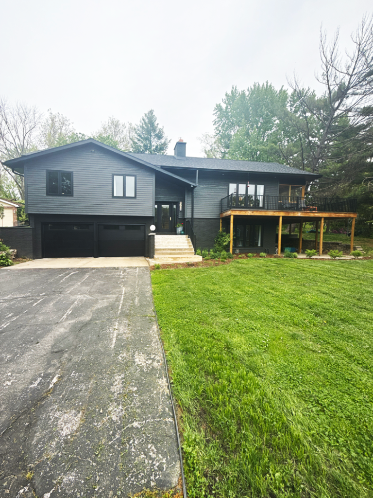 Dark gray two-story house with a black garage, front steps, and a large deck above the yard