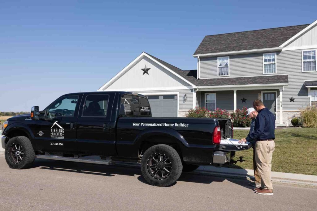 Two men review paperwork beside a black Yingling Builders pickup truck in front of a house