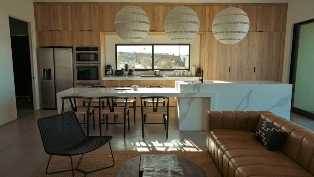 Modern open-plan kitchen and living room with wood cabinets, island seating, and a brown leather sofa