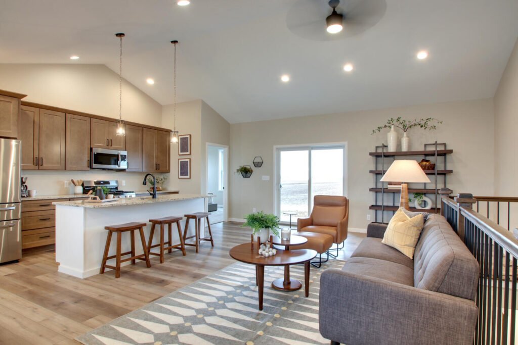 Open-concept kitchen and living room with a sofa, island stools, and a view of the water through sliding doors