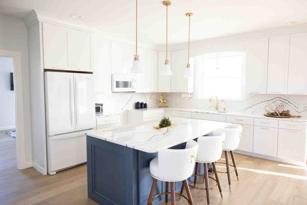 Bright modern kitchen with white cabinets, marble island, gold pendant lights, and three white bar stools