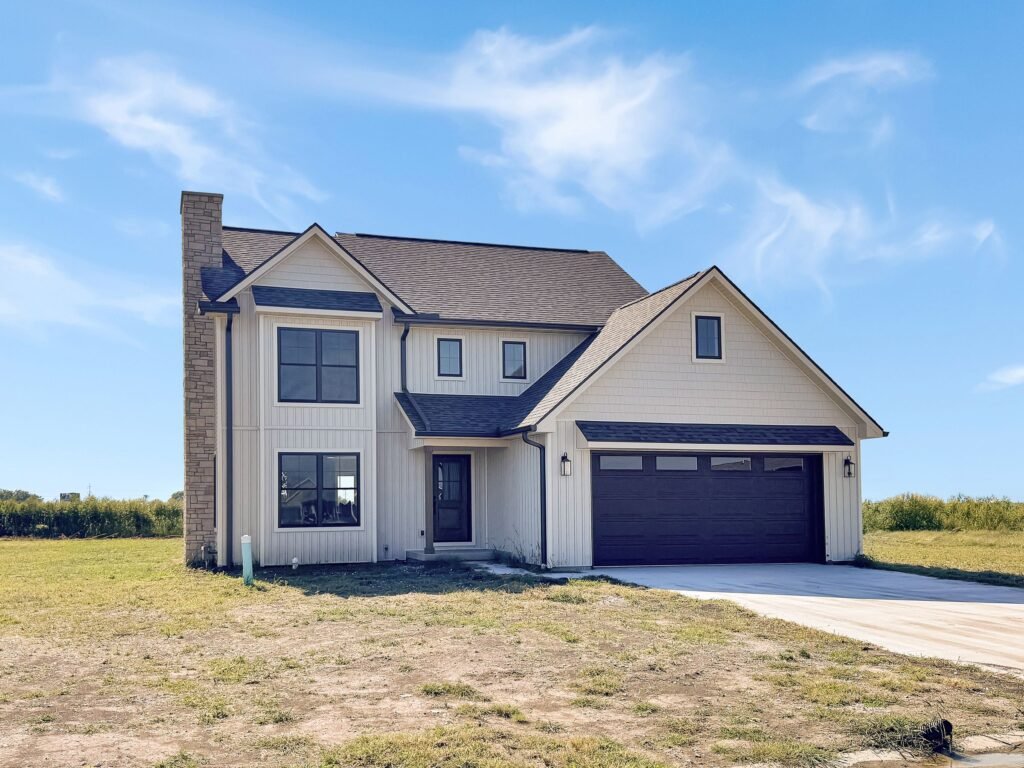 Two-story home with herringbone siding, warm beige stone, a dark roof and a two-car garage