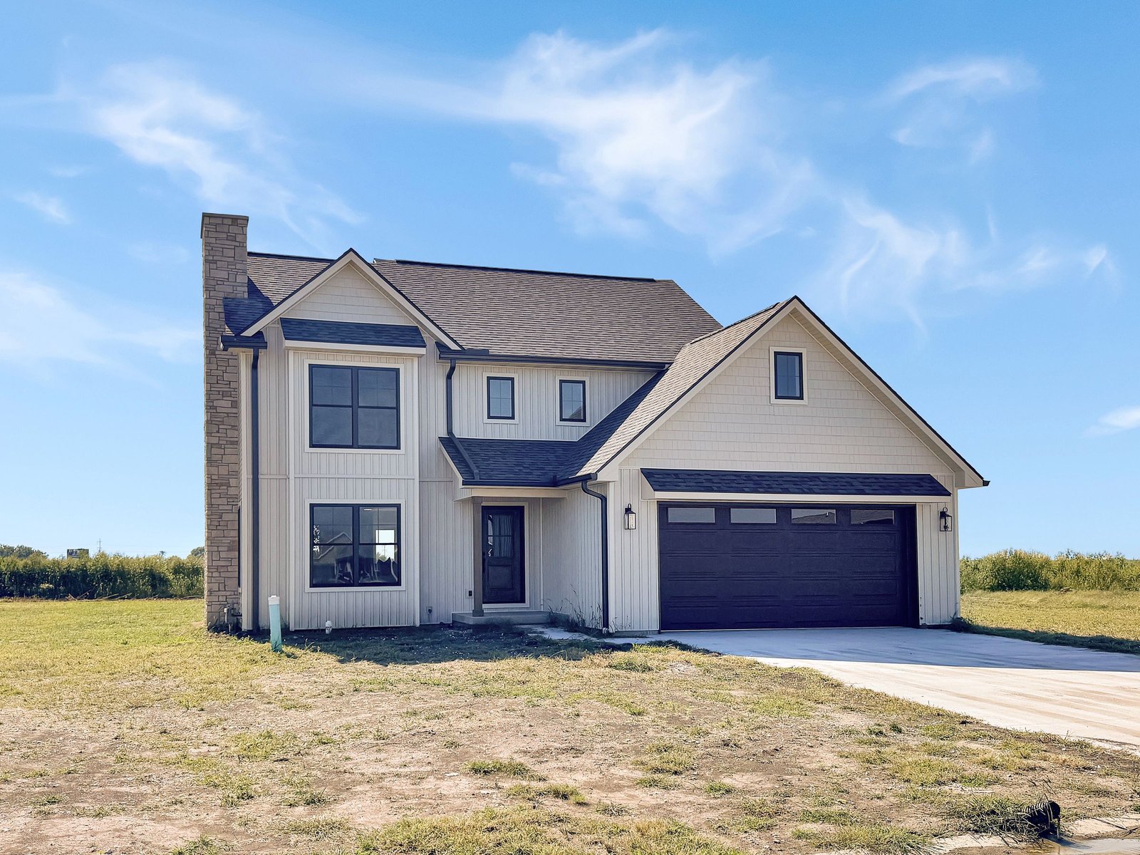 Two-story home with herringbone siding, warm beige stone, a dark roof and a two-car garage